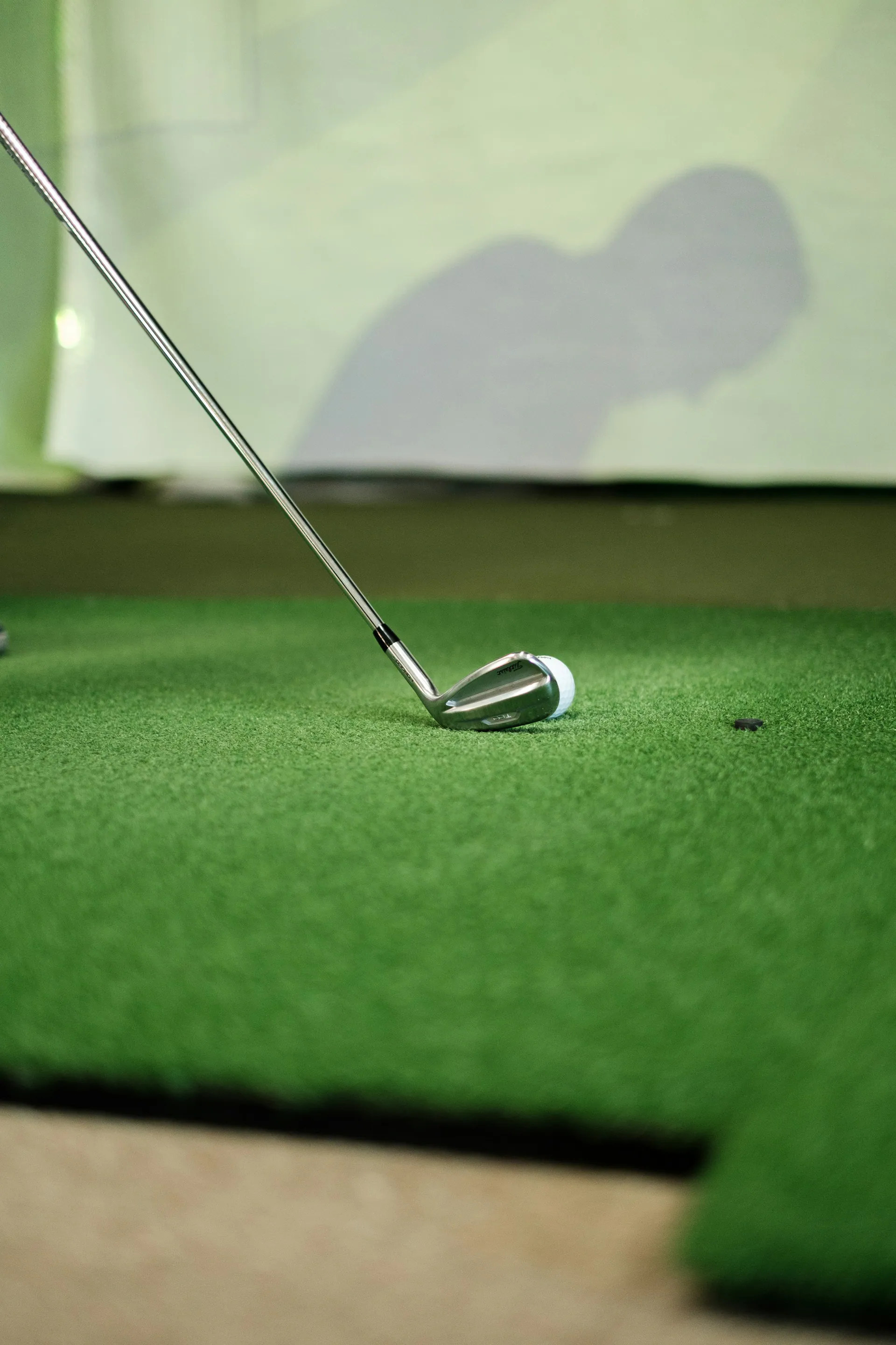Iron resting behind a golf ball on an indoor hitting mat