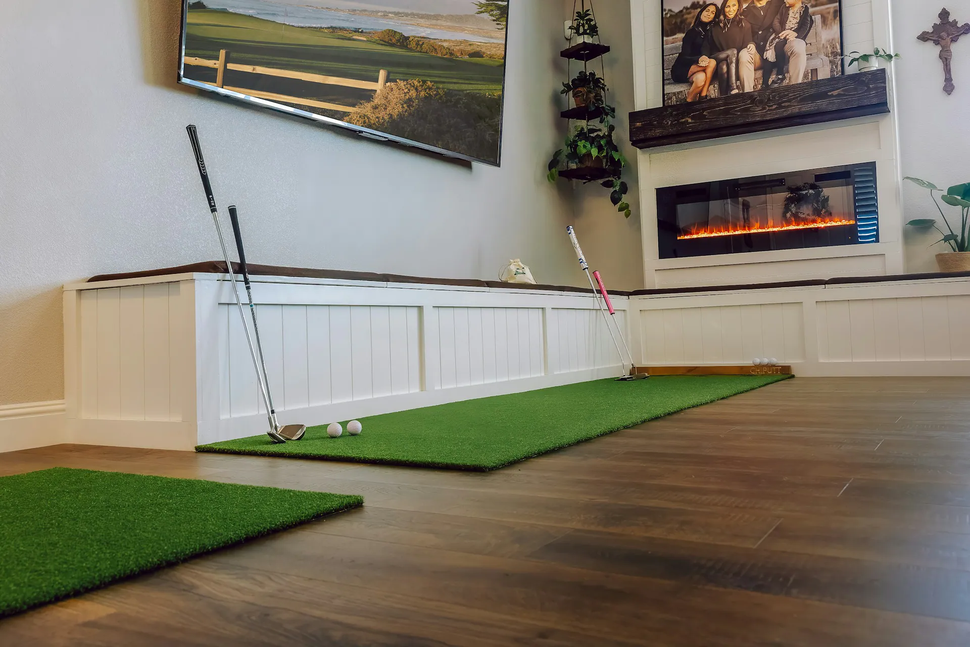 A living room golf setup with turf mats and a wall-mounted screen