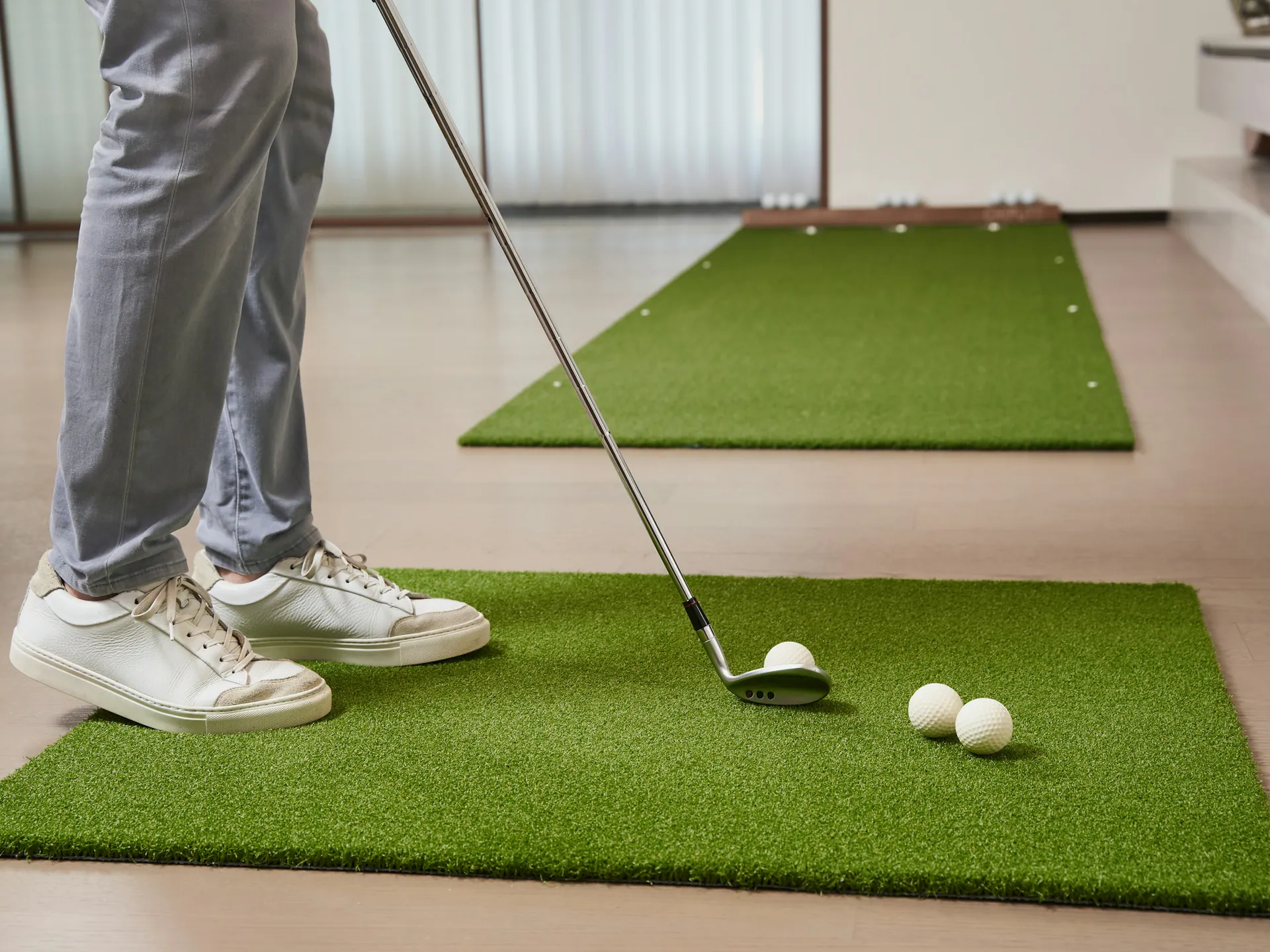 Golfer standing on an indoor hitting mat with an iron and golf balls