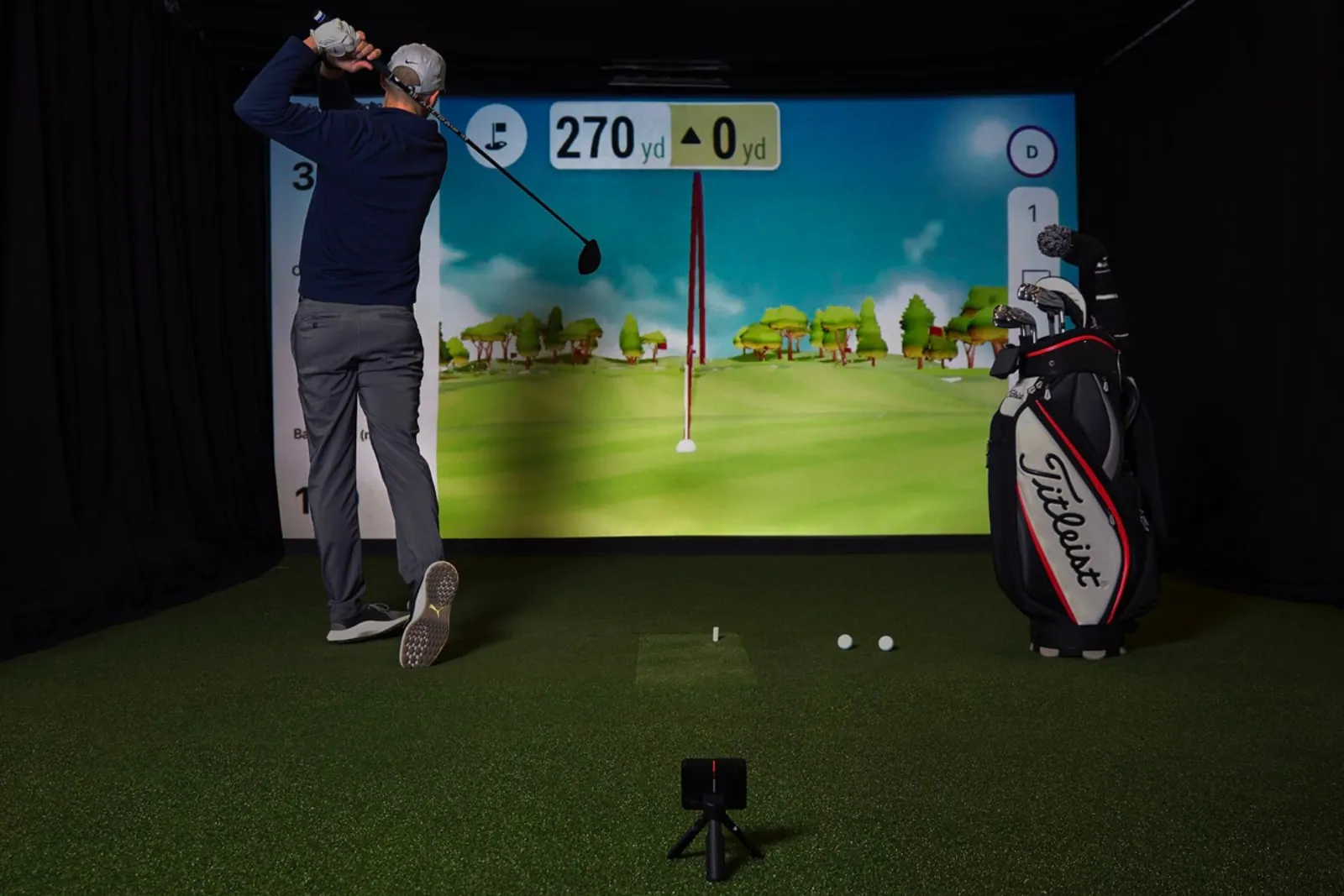 Golfer hitting into an indoor simulator screen with a Garmin Approach R10 behind the ball