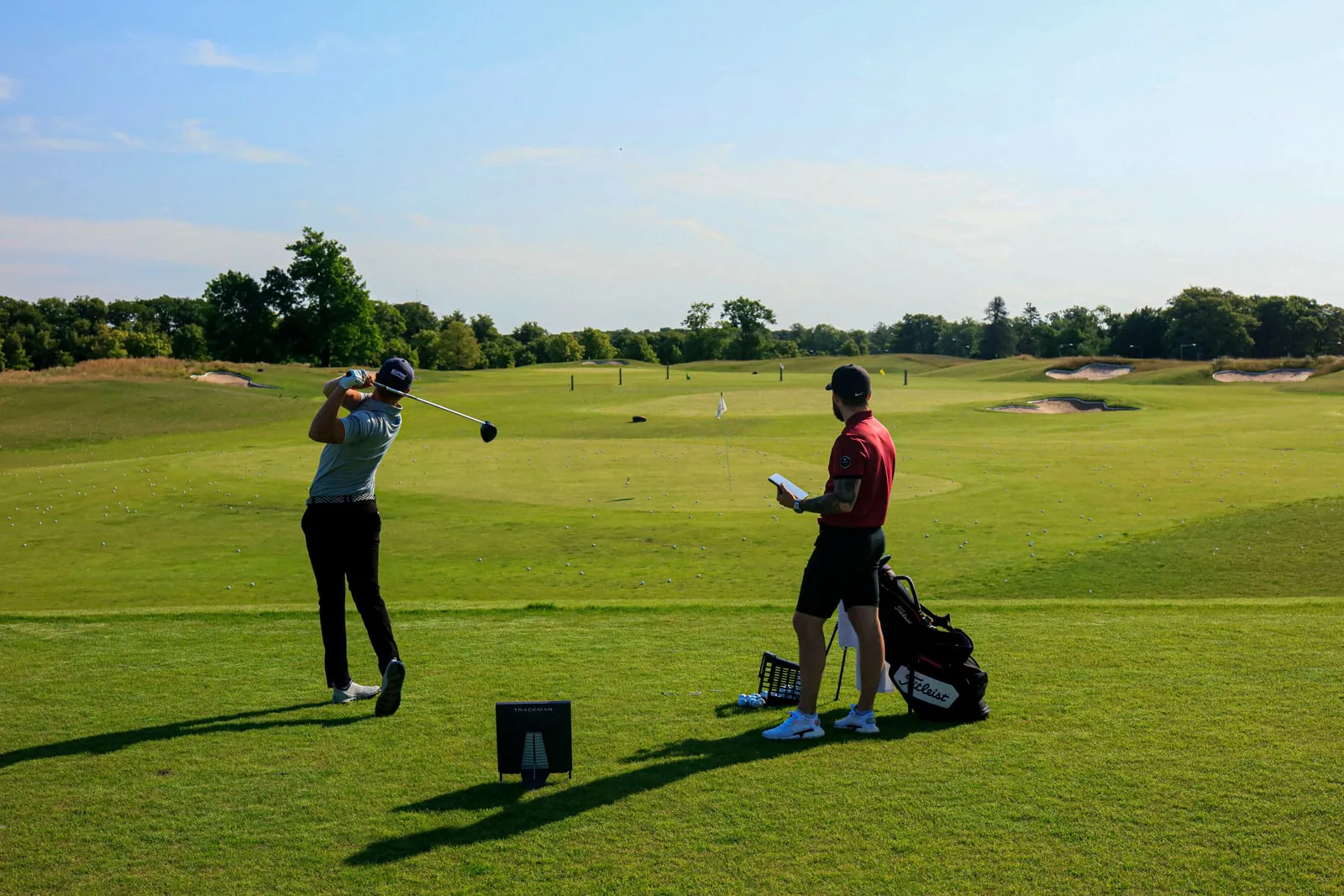 Golfer and coach on a driving range with a Trackman 4 behind the ball