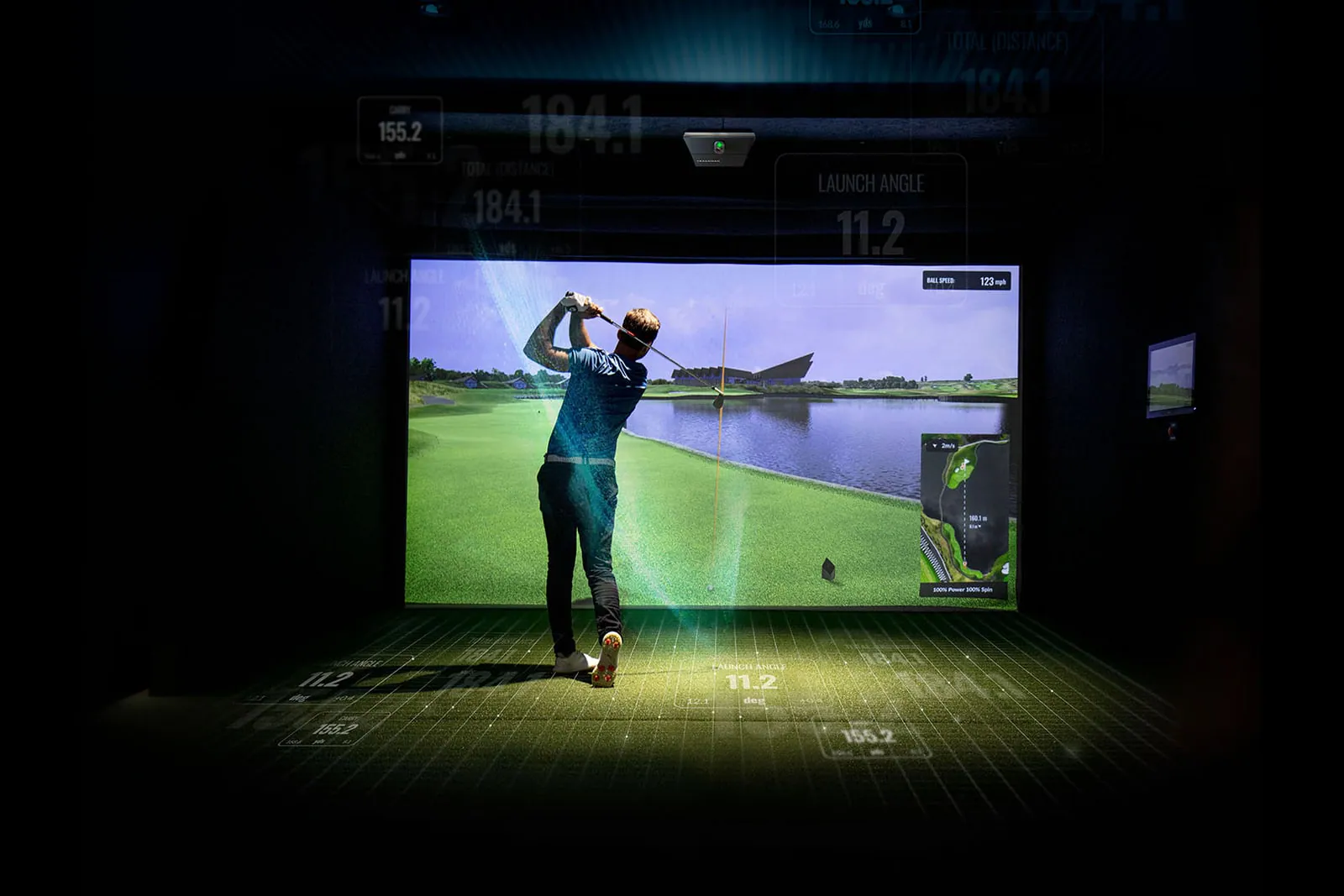 Golfer swinging in a simulator bay with a Trackman iO